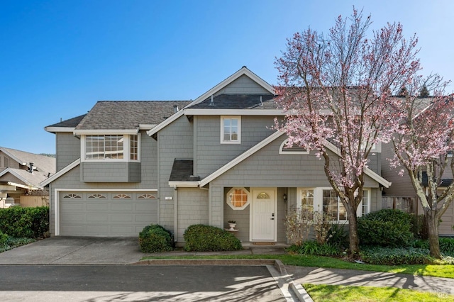 multi unit property with roof with shingles, driveway, and an attached garage