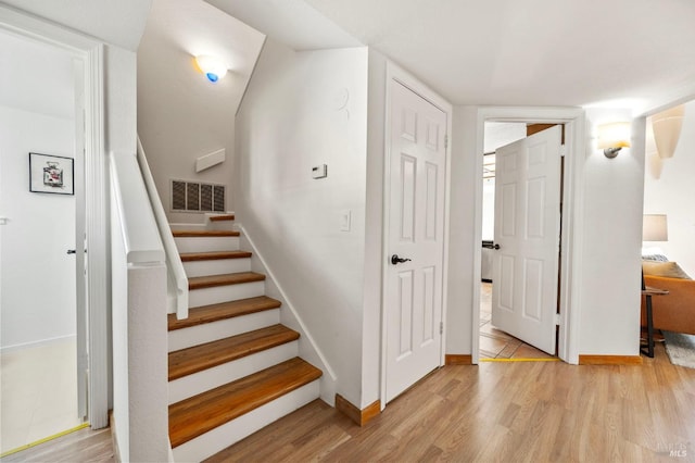 staircase featuring wood finished floors, visible vents, and baseboards