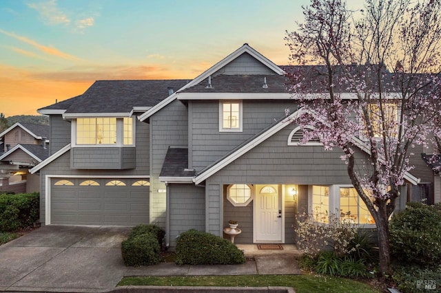 multi unit property featuring a garage, driveway, and roof with shingles