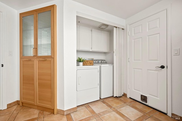 clothes washing area with cabinet space, light tile patterned floors, and washing machine and clothes dryer