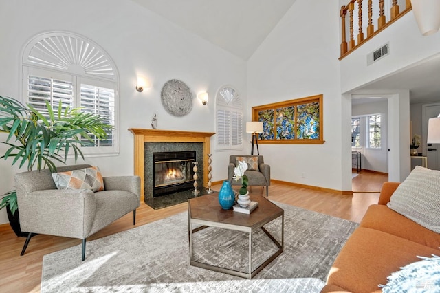 living room with visible vents, baseboards, a fireplace with flush hearth, wood finished floors, and high vaulted ceiling