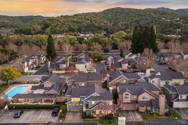 aerial view at dusk featuring a residential view and a wooded view