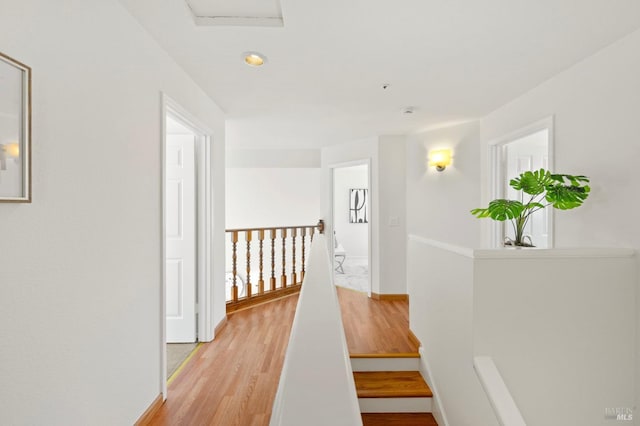 hall with light wood-type flooring, baseboards, and an upstairs landing