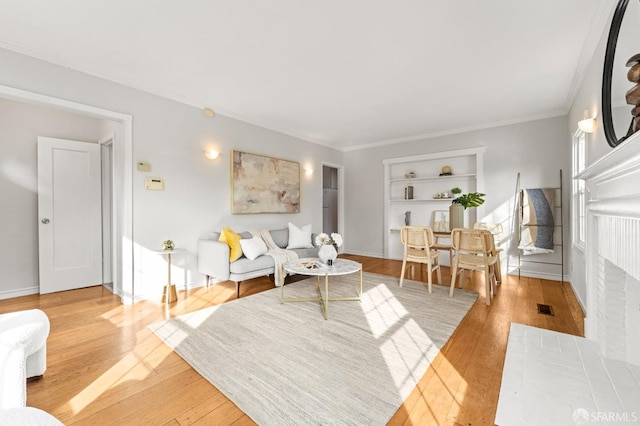 living area with baseboards, visible vents, ornamental molding, light wood-style floors, and built in shelves