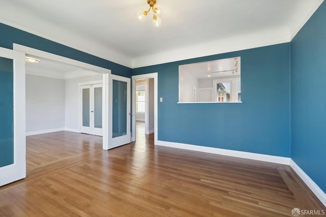 unfurnished room with french doors, a notable chandelier, crown molding, and hardwood / wood-style floors