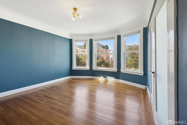 empty room featuring wood-type flooring and a notable chandelier