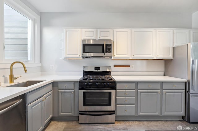 kitchen with appliances with stainless steel finishes, white cabinetry, sink, and gray cabinets