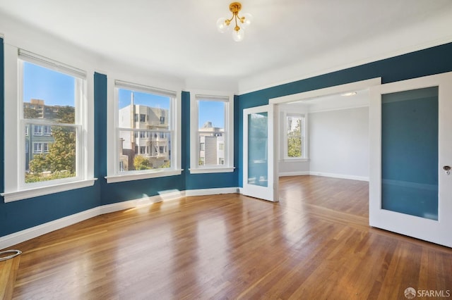 empty room featuring an inviting chandelier, a wealth of natural light, and wood-type flooring