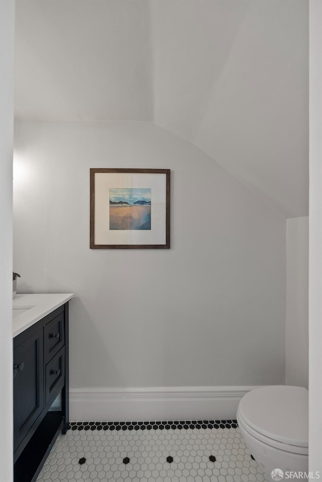 bathroom with vaulted ceiling, toilet, vanity, and tile patterned flooring