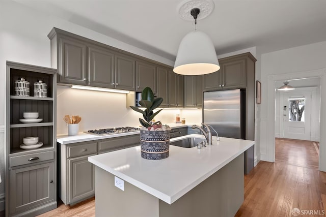 kitchen featuring decorative light fixtures, stainless steel appliances, light hardwood / wood-style floors, sink, and a kitchen island with sink