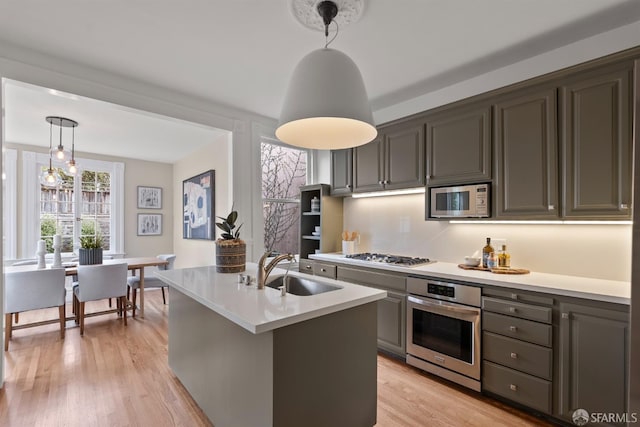 kitchen with pendant lighting, light hardwood / wood-style flooring, sink, a kitchen island with sink, and stainless steel appliances