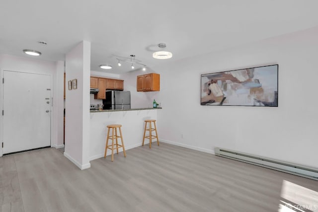 kitchen with stainless steel refrigerator, a kitchen breakfast bar, light hardwood / wood-style floors, a baseboard radiator, and kitchen peninsula