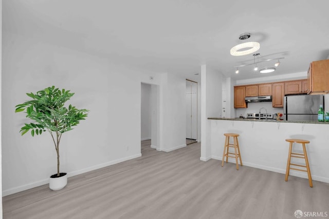 kitchen with stainless steel refrigerator, a breakfast bar, kitchen peninsula, and light hardwood / wood-style flooring