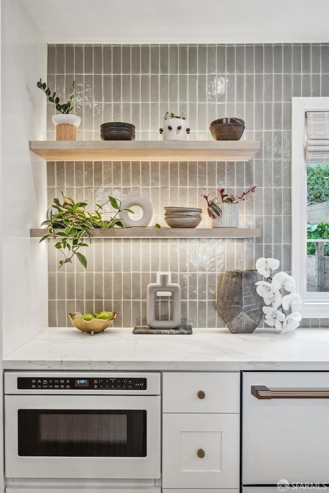 bar with tasteful backsplash, light stone counters, dishwasher, oven, and white cabinets