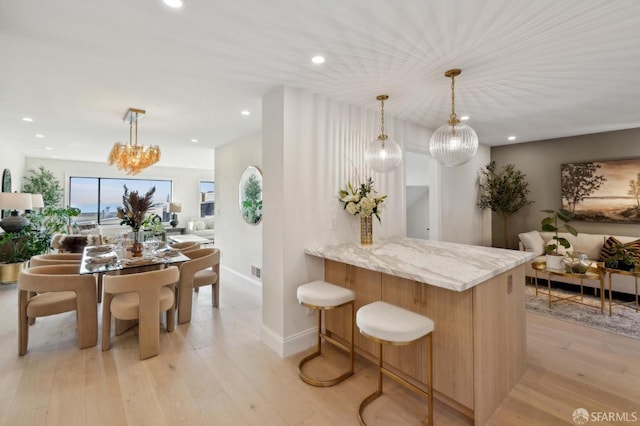 kitchen with hanging light fixtures, light hardwood / wood-style floors, kitchen peninsula, and light stone countertops