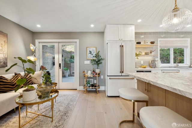 interior space with light hardwood / wood-style flooring, white cabinetry, hanging light fixtures, light stone counters, and high end refrigerator