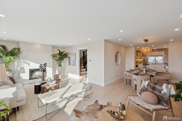 living room with sink, an inviting chandelier, a fireplace, and light hardwood / wood-style floors