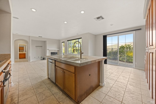 kitchen featuring stainless steel dishwasher, a wealth of natural light, sink, a tile fireplace, and an island with sink