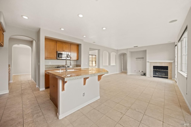 kitchen with a center island with sink, a kitchen breakfast bar, sink, light stone countertops, and light tile patterned floors