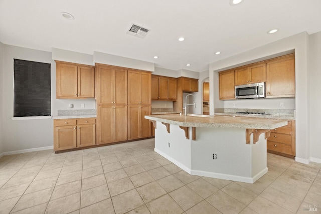 kitchen featuring stainless steel appliances, sink, an island with sink, a breakfast bar area, and light tile patterned flooring