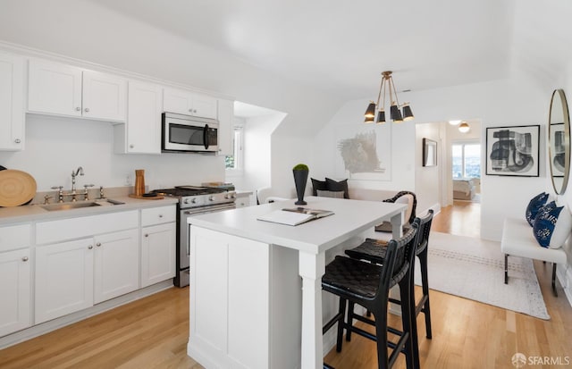 kitchen featuring white cabinets, appliances with stainless steel finishes, a center island, light countertops, and a sink