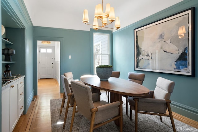 dining room with baseboards, ornamental molding, an inviting chandelier, and light wood-style floors