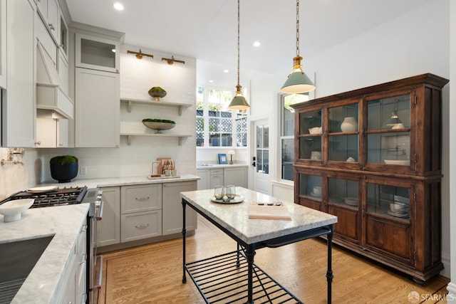 kitchen with tasteful backsplash, decorative light fixtures, light stone countertops, light wood-type flooring, and stainless steel range with gas stovetop