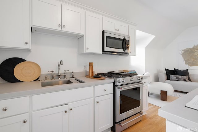 kitchen featuring light countertops, light wood-style flooring, appliances with stainless steel finishes, white cabinets, and a sink