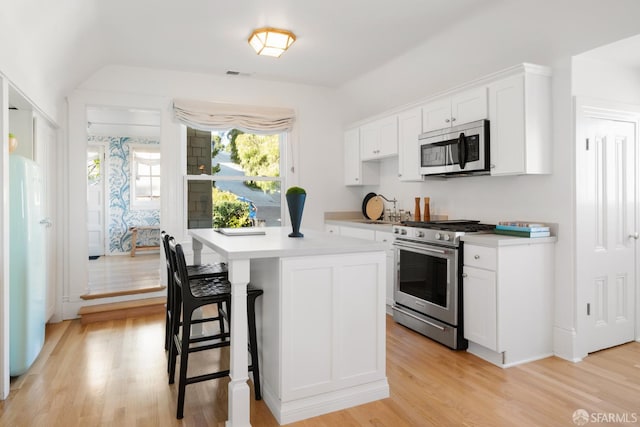 kitchen with white cabinets, a breakfast bar, stainless steel appliances, light countertops, and light wood-style floors