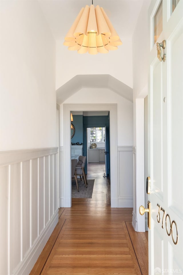 corridor featuring light wood-style floors, a decorative wall, and wainscoting