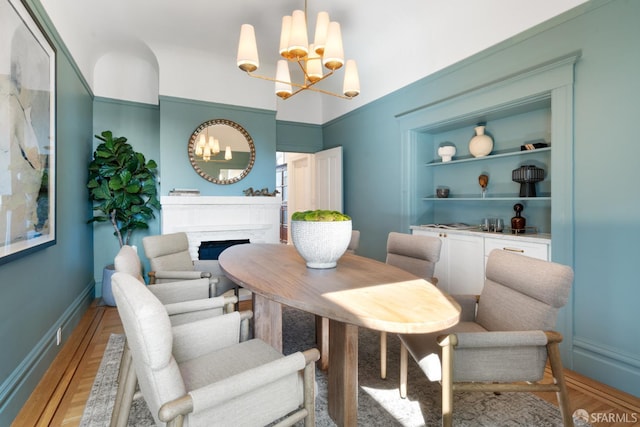 dining room featuring a chandelier, a fireplace, baseboards, built in features, and light wood-type flooring