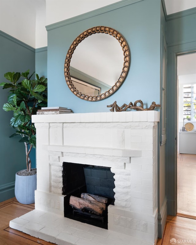 interior details featuring a brick fireplace, crown molding, and wood finished floors