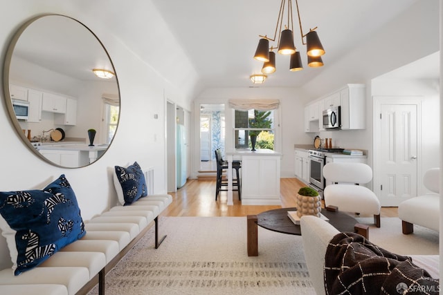 living room with a notable chandelier, vaulted ceiling, and light wood-style flooring