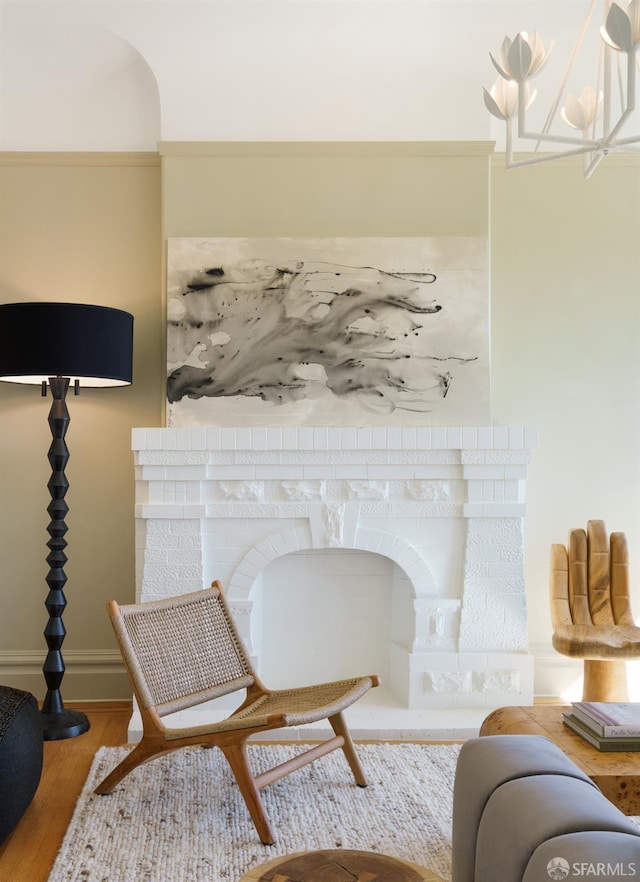 sitting room featuring a brick fireplace, baseboards, an inviting chandelier, and wood finished floors