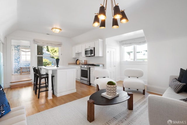 interior space featuring light wood finished floors, appliances with stainless steel finishes, a breakfast bar area, a center island, and white cabinetry