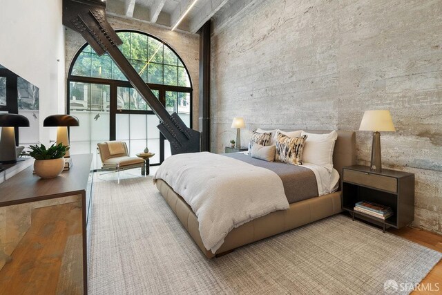 bedroom featuring beamed ceiling, wood-type flooring, and a high ceiling