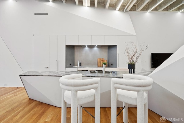 kitchen featuring a towering ceiling, light hardwood / wood-style floors, white cabinetry, and sink