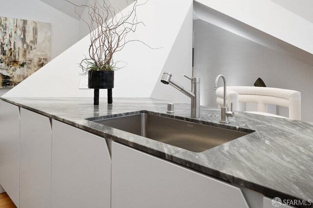 interior details with dark stone countertops, sink, and white cabinets