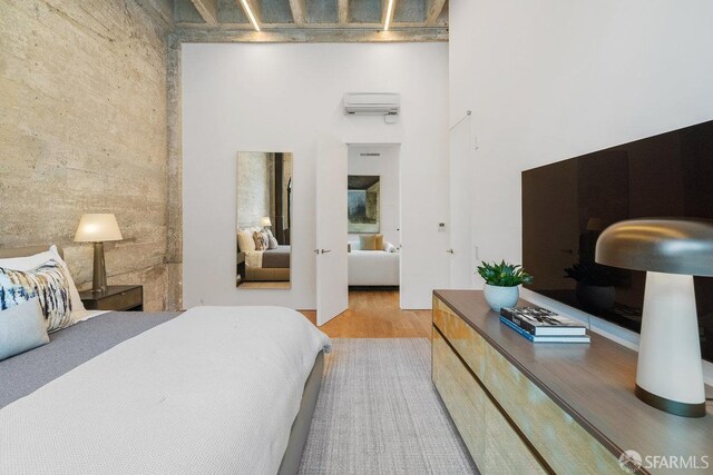 bedroom with an AC wall unit, a high ceiling, and hardwood / wood-style flooring