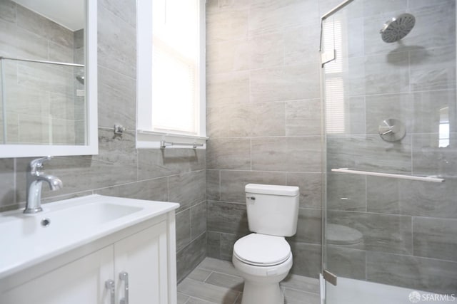 bathroom featuring vanity, toilet, tile walls, and a tile shower