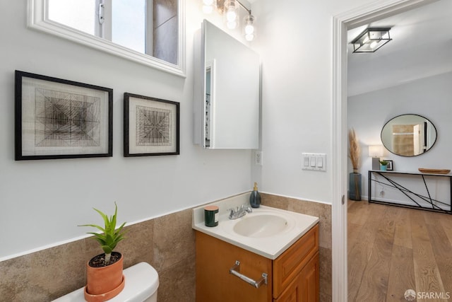 bathroom with hardwood / wood-style flooring, vanity, tile walls, and toilet