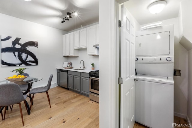 kitchen with sink, white cabinetry, stainless steel appliances, stacked washer / drying machine, and light wood-type flooring