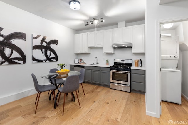 kitchen with sink, stacked washing maching and dryer, white cabinetry, gray cabinetry, and stainless steel gas range oven