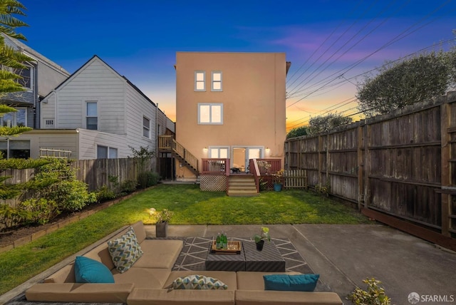 back of house at dusk with stucco siding, a fenced backyard, a deck, an outdoor living space, and a yard