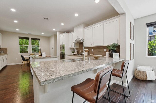 kitchen with stainless steel appliances, white cabinetry, light stone counters, tasteful backsplash, and dark wood-type flooring