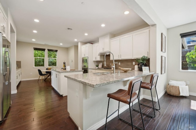 kitchen with appliances with stainless steel finishes, kitchen peninsula, light stone countertops, white cabinets, and sink