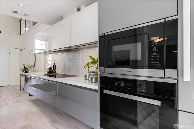229 8th St Unit 3, San Francisco, CA 94103 - kitchen with black appliances, modern cabinets, tasteful backsplash, white cabinets, and light wood-type flooring