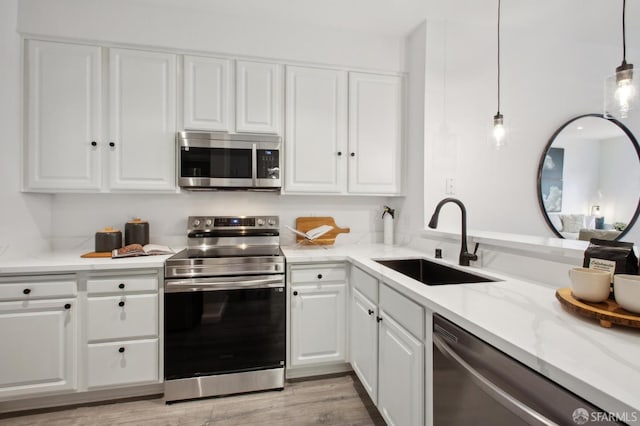 kitchen with pendant lighting, sink, stainless steel appliances, light stone counters, and white cabinets