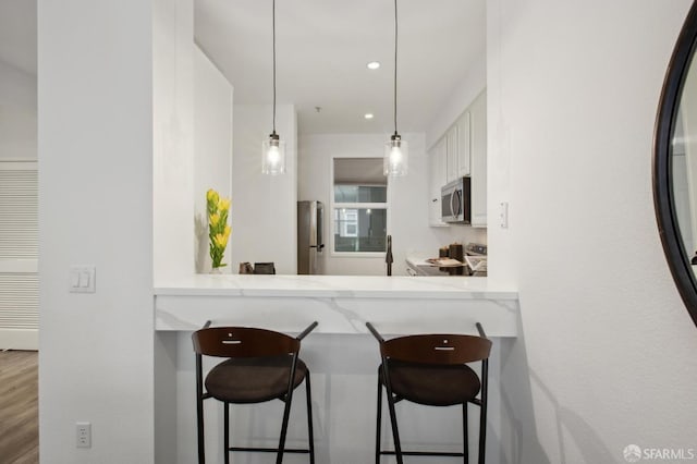 kitchen with white cabinetry, a breakfast bar area, hanging light fixtures, kitchen peninsula, and stainless steel appliances