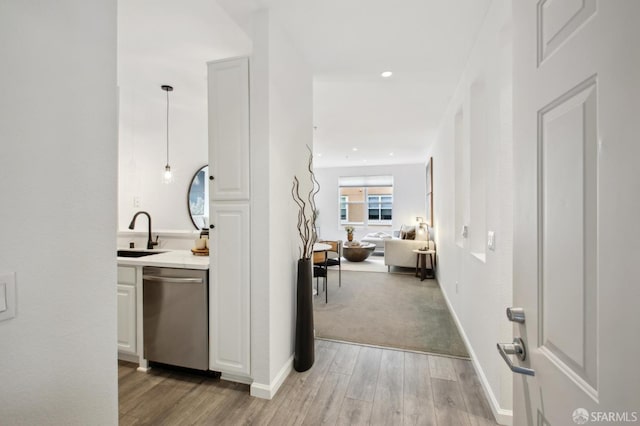 interior space with sink, dishwasher, hanging light fixtures, light hardwood / wood-style floors, and white cabinets